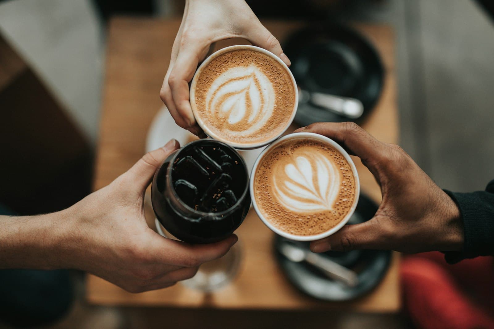 Three friends raising coffee cups together over a café table